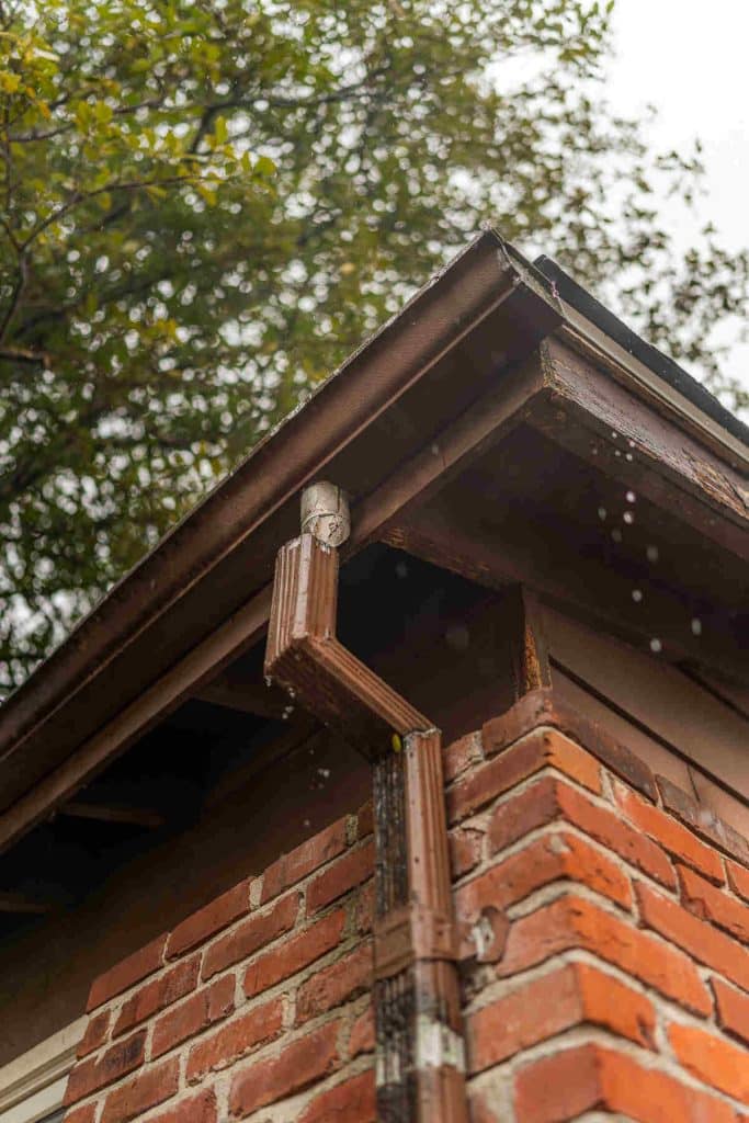 A gutter with rain water falling from it entering the basement of a homeowner.
