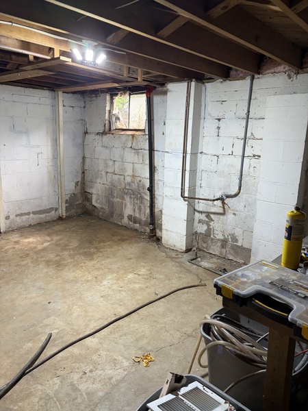 Before foundation repair and basement waterproofing in Roeland Park, KS, showing concrete block foundation walls with visible cracking, moisture staining, and an unfinished basement with exposed ceiling joists.