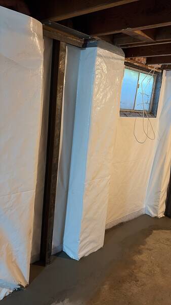 After basement waterproofing and foundation repair in Roeland Park, KS, showing a white wall vapor barrier system installed over foundation walls with steel support beams reinforcing the structure.
