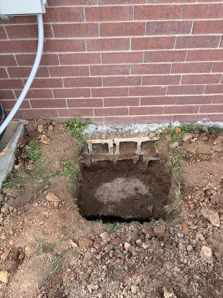 Excavation beside a brick home exposing a concrete block foundation and footing area, prepared for foundation repair work and structural support installation.