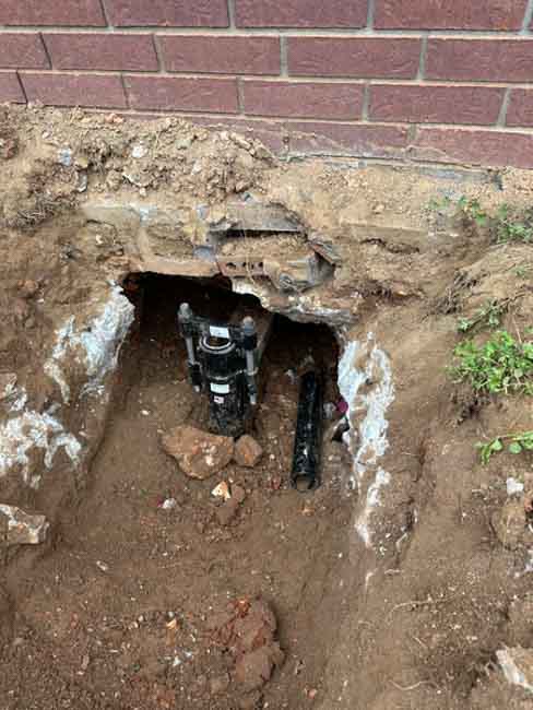 Foundation repair pier installed beneath an excavated brick home foundation, with soil removed to expose the footing and support system during stabilization work.