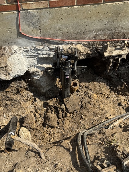 Helical pier bracket installed beneath a settling foundation in Columbia, MO, with excavation exposing the foundation footing during foundation repair by Spartan Ram Jack.