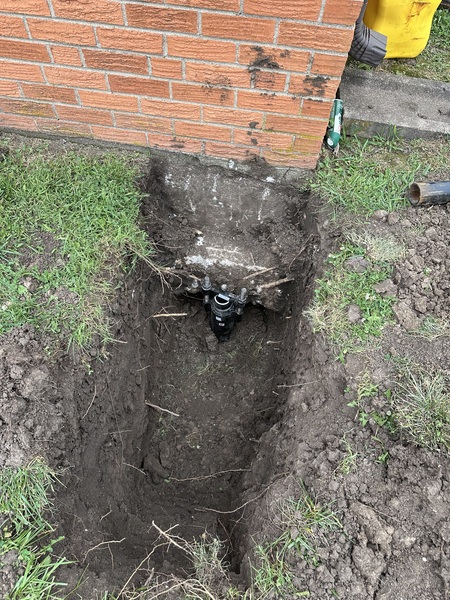 Helical pier installed beneath the corner of a church foundation in McPherson, KS, showing an excavated footing and steel foundation bracket during stabilization work by Spartan Ram Jack of Wichita.