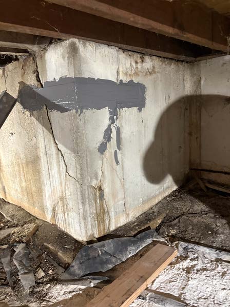After foundation repair image showing a cracked concrete crawl space wall reinforced with gray epoxy repair material beneath wood floor framing.