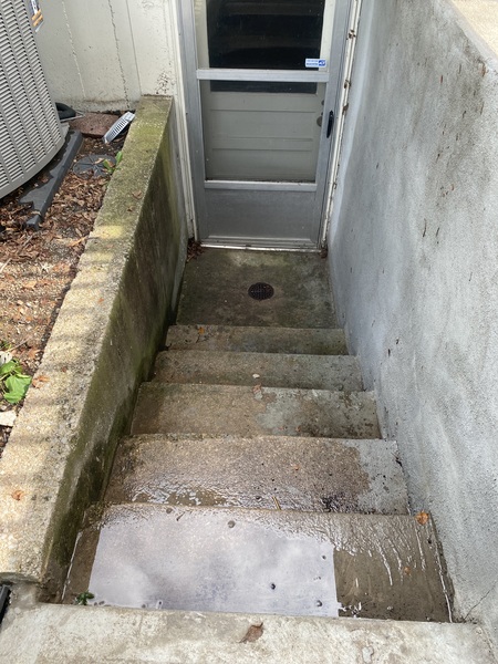 Exterior basement walkout stairwell in an Overland Park, KS home showing standing water at the landing and drainage concerns before waterproofing repairs by Spartan Ram Jack of Kansas City.