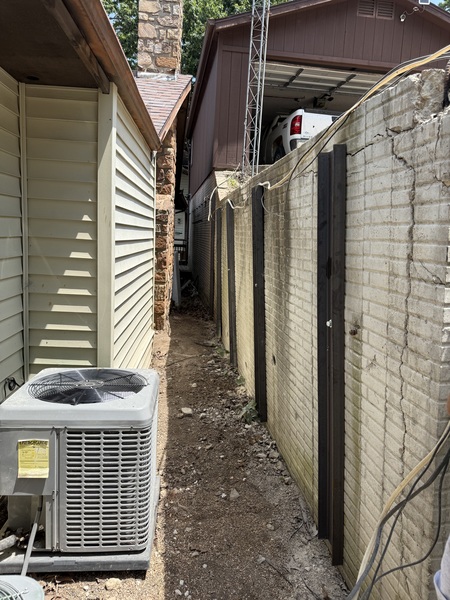 Vertical steel beams installed along a block retaining wall between two homes for earth anchor stabilization by Spartan Ram Jack.