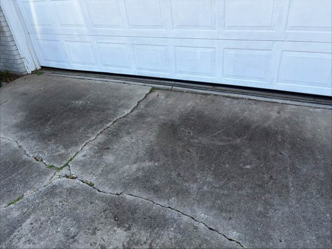 Cracked concrete driveway in front of a white garage door, showing multiple visible fractures and settlement-related damage across the slab.
