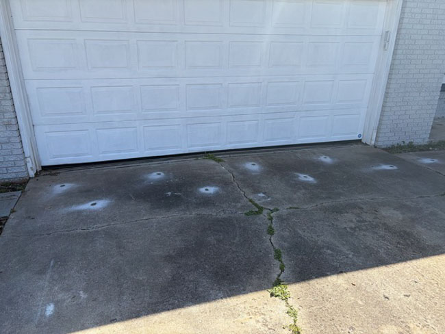 Concrete driveway in front of a white garage door with visible cracks and newly drilled injection points used for concrete lifting and stabilization.