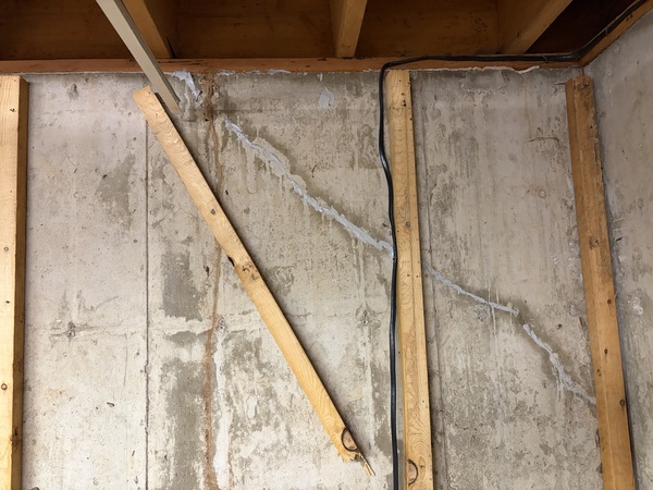 Basement foundation wall in a Springfield, MO home showing a long diagonal crack extending across poured concrete between exposed wall studs before crack injection repair by Spartan Ram Jack Springfield.