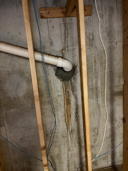 Basement foundation wall in a Springfield, MO home showing a vertical wall crack and water staining beneath a sewer pipe penetration before crack repair and waterproofing services by Spartan Ram Jack Springfield.