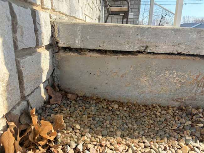 Close-up of a separated concrete porch slab next to a stone veneer foundation, showing a visible gap caused by foundation settlement at a home in Springfield, MO.