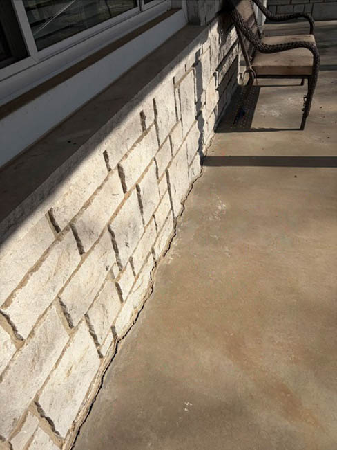 Horizontal cracking and separation along a stone veneer foundation wall beside a concrete patio, indicating foundation settlement at a home in Springfield, MO.