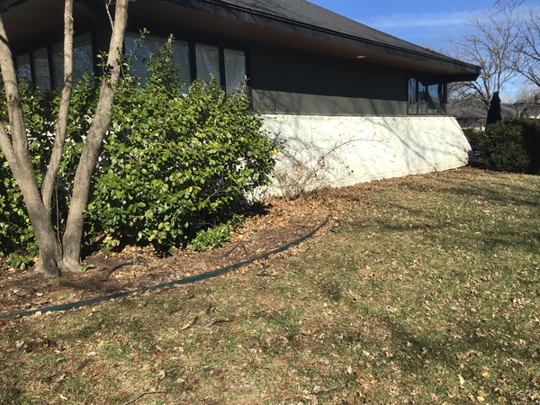 Exterior wide shot of a single-story residential home in Wichita, KS, featuring a white stone-veneered foundation undergoing inspection by Spartan Ram Jack.