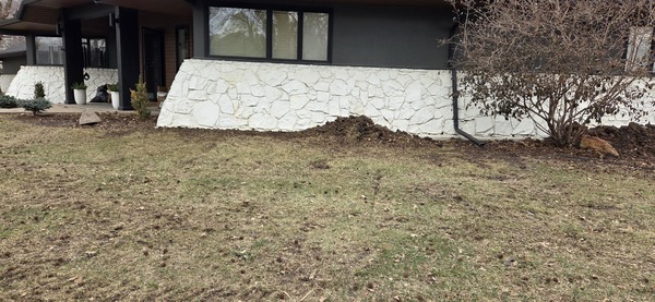 Excavation dirt piles along a residential white stone foundation during pier installation by Spartan Ram Jack in Wichita, KS.