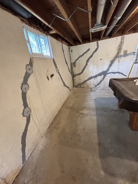 Multiple branching cracks across basement walls with patched anchor points visible on the left wall at a home in Excelsior Springs, MO.